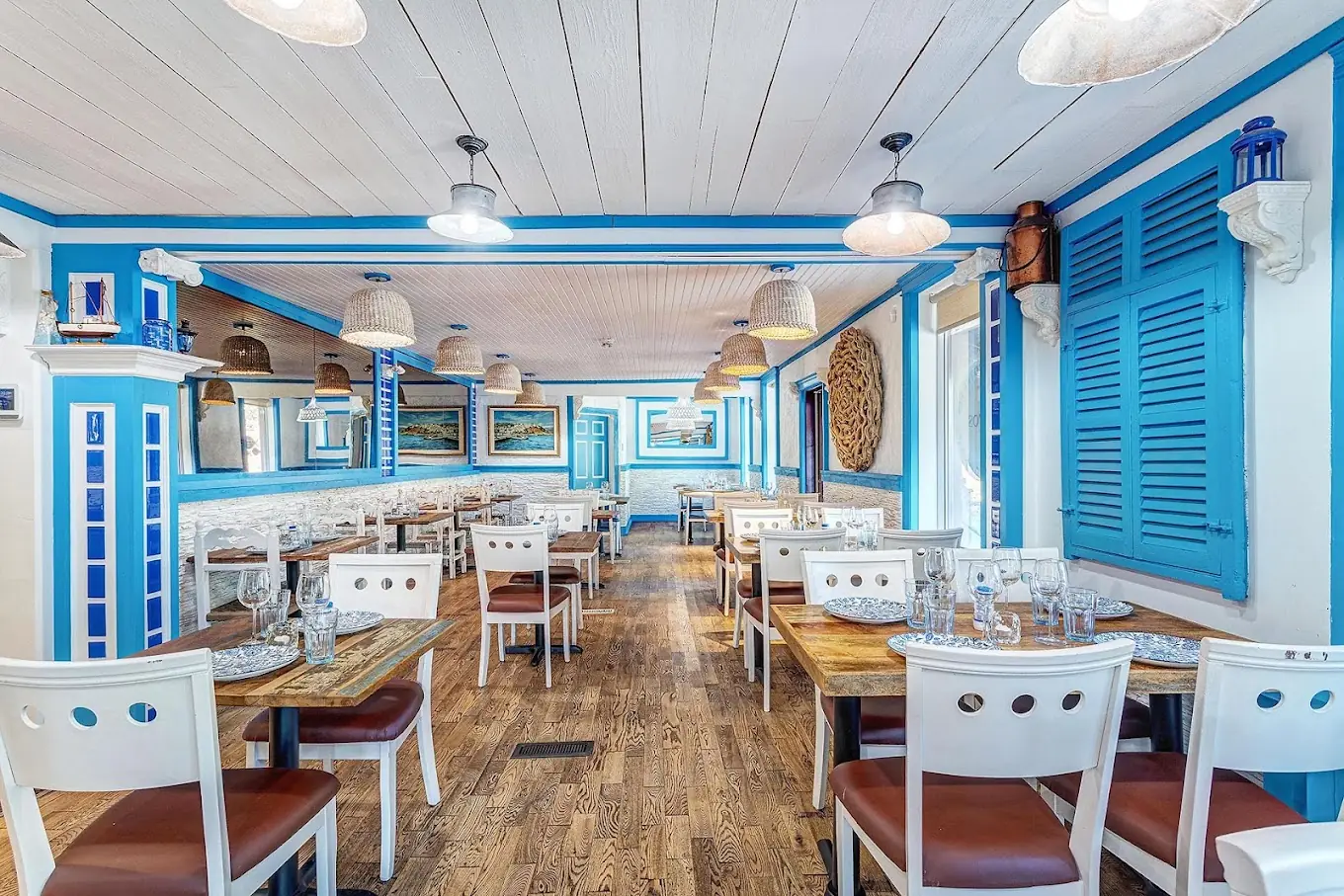 Salle de la taverne Petros le soir : décor bleu et blanc, mobilier en bois, éclairage suspendu méditerranéen, tables dressées.